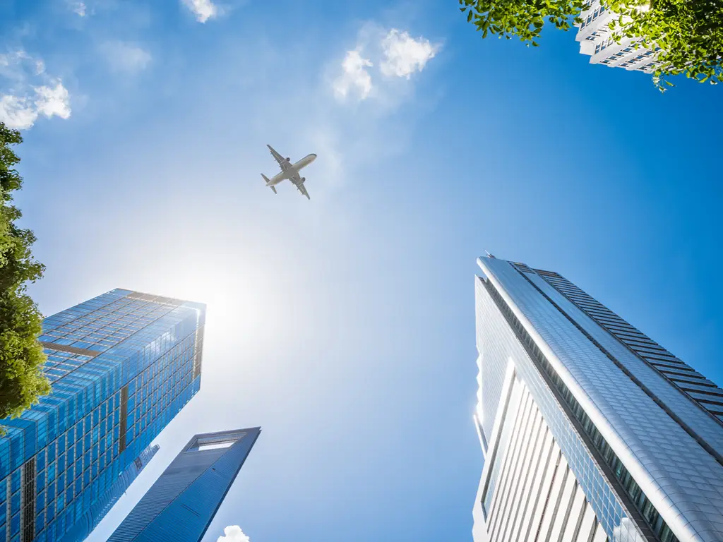 Avião de passageiros a sobrevoar uma cidade moderna sob um céu azul límpido.